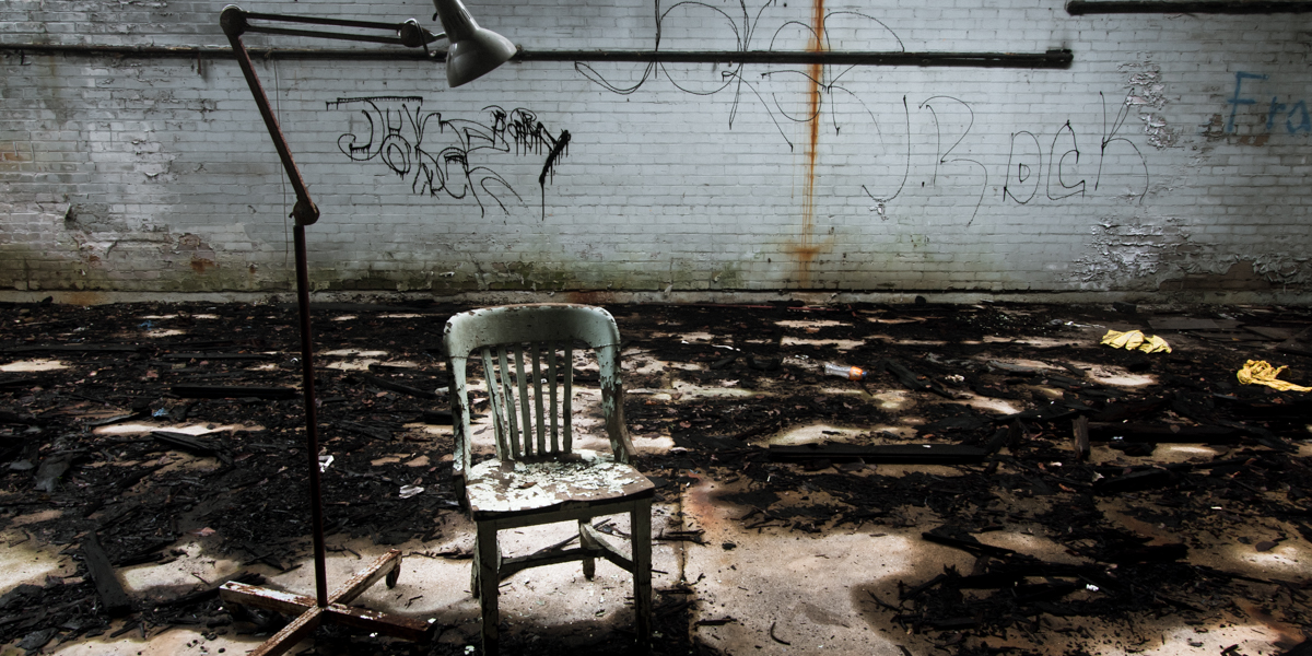 Chair and floor lamp in a ruined Detroit factory interior, conveying the feeling of an interrogation place in the middle of some dark hall, where some poor soul has been interrogated, or beaten, or worse